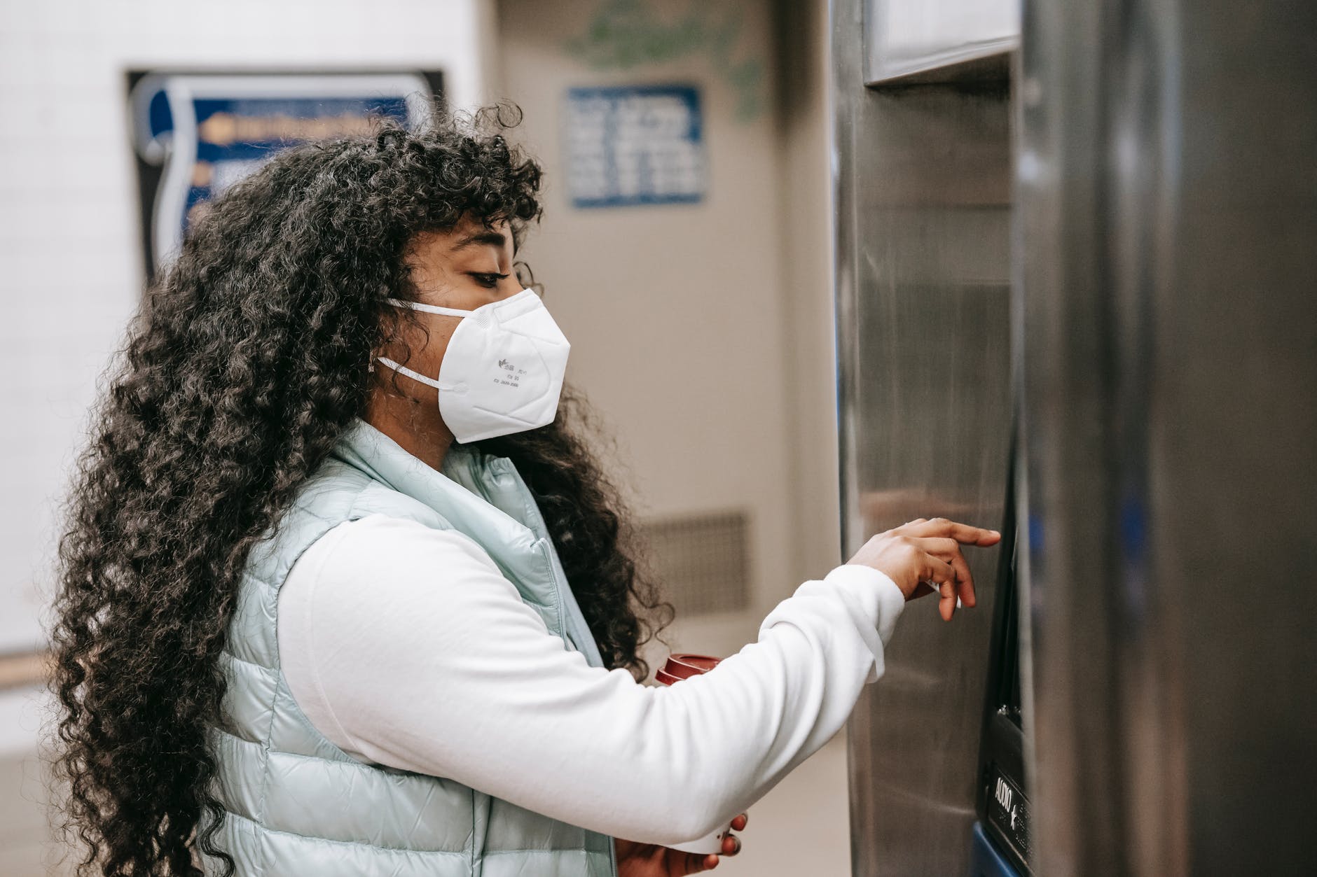 focused black woman in respirator using atm or ticket machine